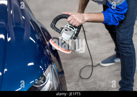 professional mechanic using a power buffer machine for cleaning the body of a car from scratches. Stock Photo