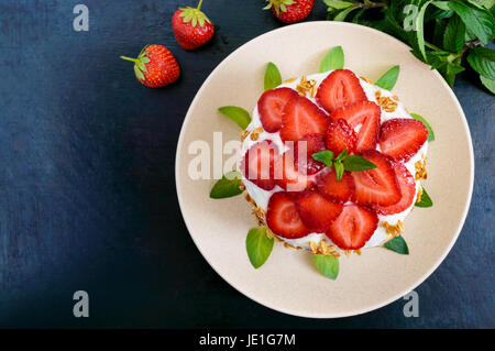 A festive cake with fresh strawberries, cream, decorated with mint leaves on a black background. Top view. Close-up. Stock Photo