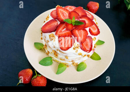 A festive cake with fresh strawberries, cream, decorated with mint leaves on a black background. Top view. Stock Photo