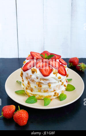 A festive cake with fresh strawberries, cream, decorated with mint leaves on a black background. Vertical view Stock Photo