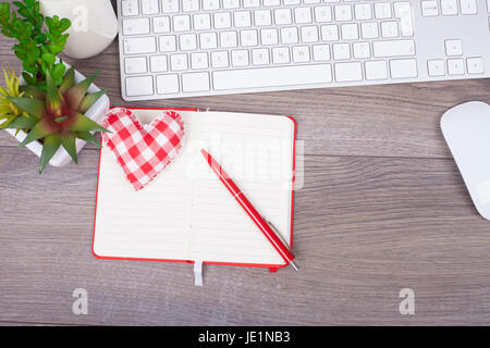 Work desk with keyboard, open note, pen and beautiful heart of textiles. With empty space for your text. View from above Stock Photo