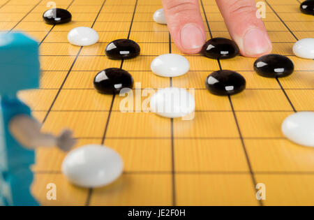 fingers placing piece of GO on board with a robot in front, concept of human against robot Stock Photo