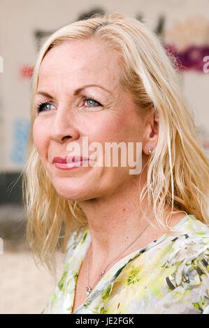 seitliches Kopf-und-Schulter-Porträt einer blonden Frau mittleren Alters vor einer bemalten Wand lächelnd zur Seite blickend Stock Photo