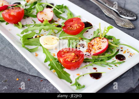 Fresh radish, cherry tomato, quail egg, rucola with balsamic glaze on a white plate. Mediterranean lifestyle. Healthy food. Selective focus Stock Photo