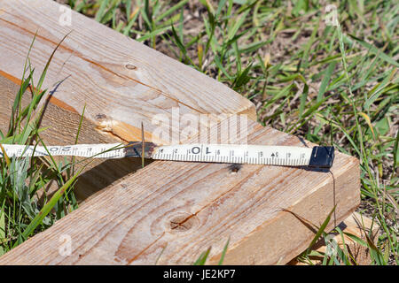 Construction wooden cottage. Measuring pine bars with the help of a vintage yardstick tool outdoor closeup. Stock Photo