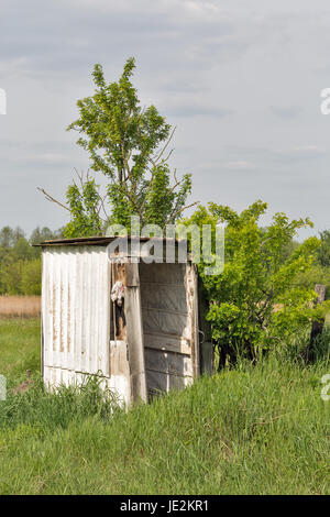 Old wooden dilapidated toilet camping in a village among the trees and bushes. Stock Photo