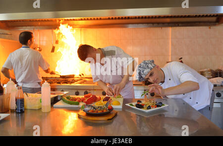 Handsome chef dressed in white uniform decorating pasta salad and seafood fish in modern kitchen Stock Photo