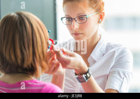 Optometry concept - pretty, young female optometrist examining her patient's eyes, finding the optimal correction to achieve optimal sight Stock Photo