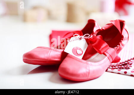 Gift wrapped girls red shoes with ribbon and heart tag Stock Photo