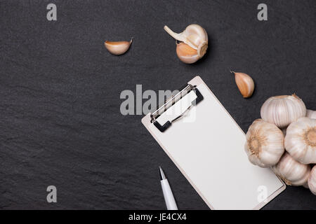 Vegetable recipe. Open menu book with garlic on dark background Stock Photo