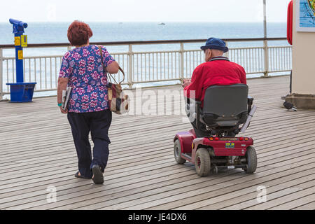 Senior couple on Bournemouth pier, man in mobility scooter at Bournemouth, Dorset in June Stock Photo