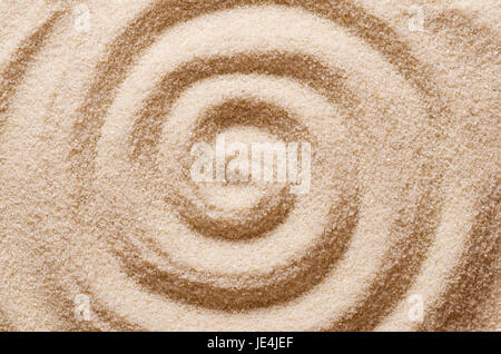 Spiral in the sand. Archimedean spiral made with the finger in dry ocherous sand. Macro photo close up from above. Stock Photo
