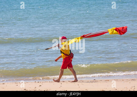 RNLI Lifeguard carrying the red and yellow flags indicating safe area to swim at the seaside on Bournemouth beach, Dorset in June