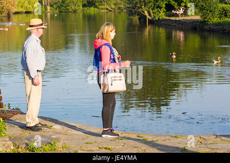 Man and woman looking out over Poole Park lake, at Poole Park, Dorset on a sunny evening in June Stock Photo