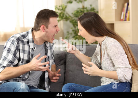 Couple arguing and screaming each other sitting on a sofa in the living room at home Stock Photo