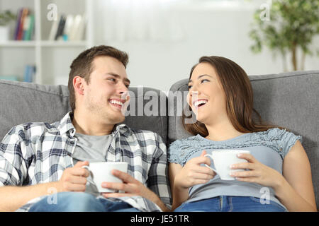 Relaxed couple talking and holding coffee cups sitting on a sofa in the living room at home Stock Photo