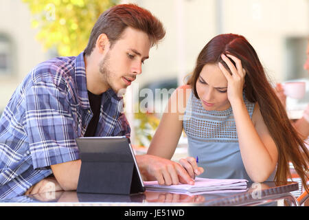 Student helping to learn a lesson to an attentive friend sitting in a restaurant table Stock Photo