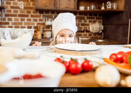 little girl making pizza dough with pizza ingredients in kitchen Stock Photo