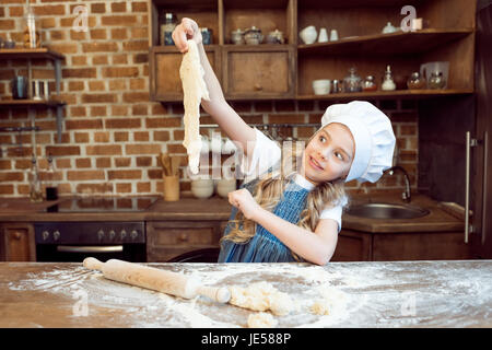 shocked little girl in chef hat looking at raw dough Stock Photo