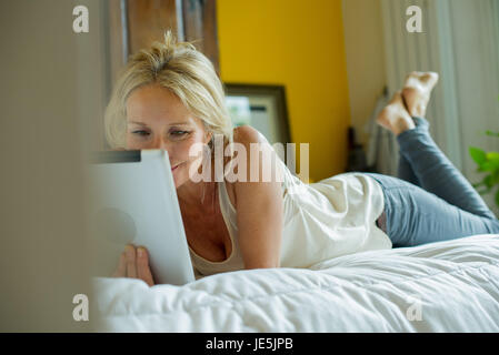 Mature woman lying on bed watching digital tablet Stock Photo