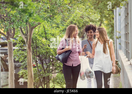 Friends chatting as they walk down sidewalk with shopping bags in hands Stock Photo