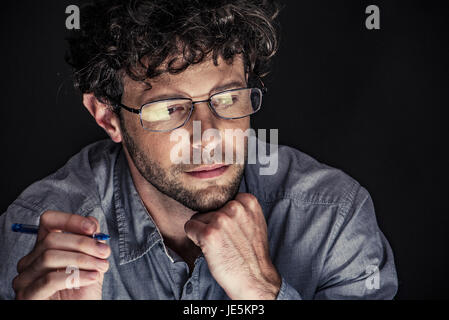 Man holding pen and looking down with hand under chin Stock Photo