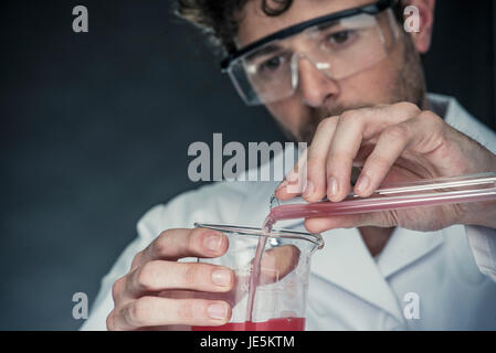 Scientist pouring liquid from test tube into beaker Stock Photo