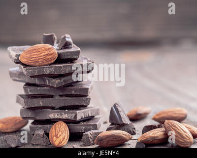 Stack of dark chocolate and whole almond with copy space. Chocolate with crumbs and almonds on wooden background. Stock Photo