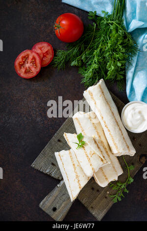 Shaurma lavash with fried chicken meat, fresh vegetables and creamy sauce on a background of brown stone. Copy space. Stock Photo