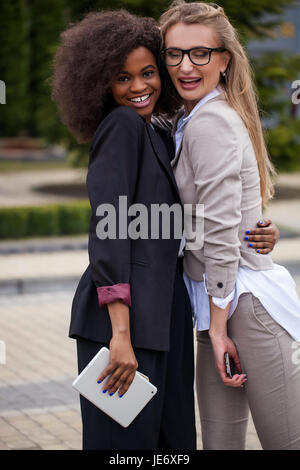 Two happy and successful businesswomen hugging in the park. Women posing for camera in suits. Stock Photo