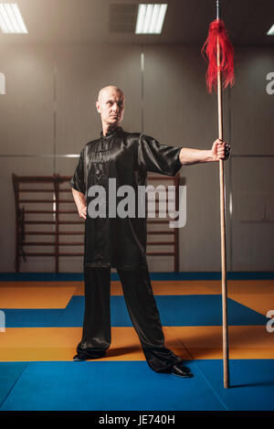 Wushu fighter poses with lance, martial arts. Man in black  cloth poses with blade Stock Photo