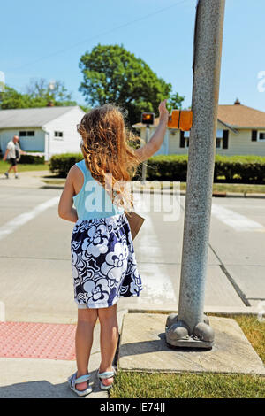 Five year old girl presses the crosswalk button as a man walks on the other side of the street in Willowick, Ohio. Stock Photo