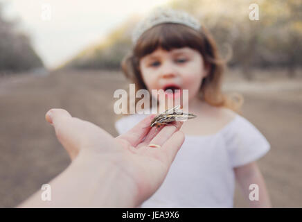Girl with tiara looking at large insect on hand Stock Photo