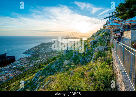 Sunset views toward the upper station of the Dubrovnik Cable Car. Tourists crowd cafes and a restaurant to watch the sun set. Stock Photo