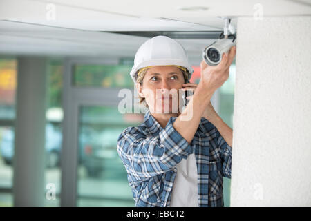 worried female technician using the phone while installing camera Stock Photo