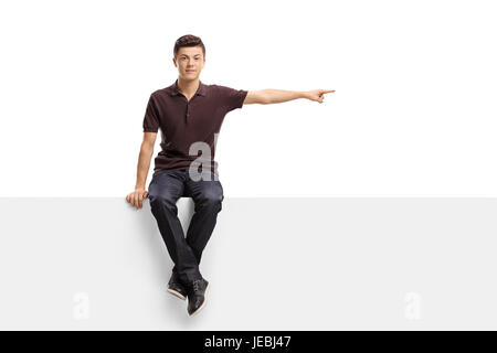 Teenage boy sitting on a panel and pointing right isolated on white background Stock Photo