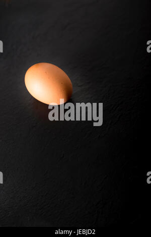 One raw egg over a black stone plate with copy space. Stock Photo