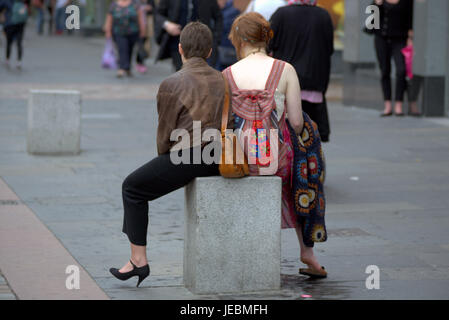 two Glasgow ladies having a rest sitting astride on a street bollard women sitting down watching life go by on Argyle Street Glasgow City centre Stock Photo