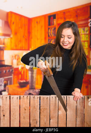 Beautiful smiling young woman cutting wood with a saw for a project Stock Photo
