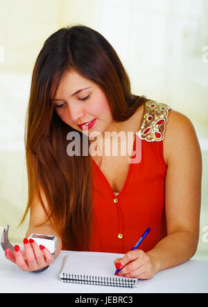 Beautiful young patient using an automatic tensiometer in her arm and taking notes of the results in his notebook, in a doctor consulting room backgro Stock Photo