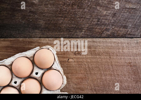 Farm fresh organic brown chicken eggs from free range chickens with in a paper carton over a rustic wooden background.