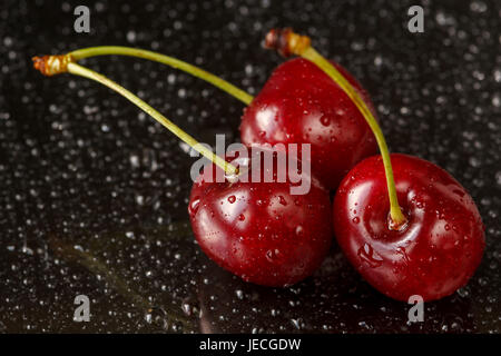 Macro shot of three delicious ripe cherries on a black reflective background with water drops. Shallow depth of field Stock Photo