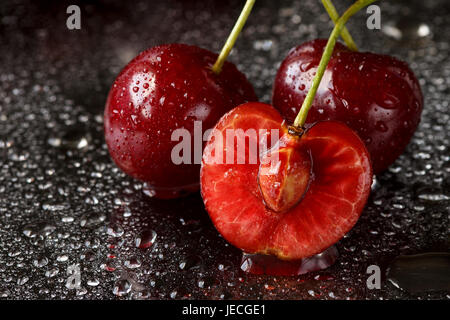 Macro of two and a half cherries on a black background with water drops. Focus on the sliced cherry Stock Photo
