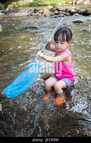 Asian Chinese little girl catching fish with fishing net in the creek. Stock Photo