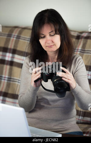 young woman transfers images from camera to white laptop pc sitting on couch Stock Photo