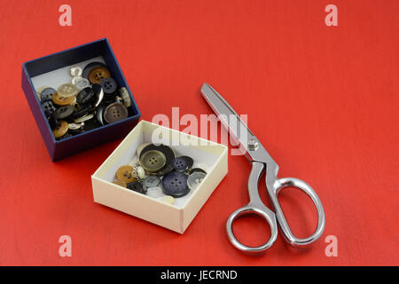 Collection of buttons in white and blue boxes and metal scissors on red wooden background Stock Photo