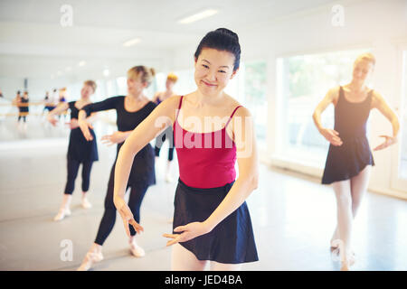 Cheerful Asian woman looking at camera practicing ballet in multiethnic group in class. Stock Photo