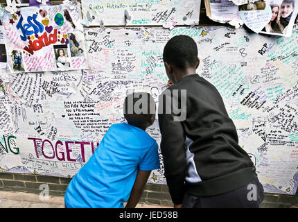 Families and friends writing on the wall of condolence in the aftermath of the fire that destroyed the 24-story Grenfell Tower in North Kensington, London on 14th June 2017.  The death toll officially at 75 but will no doubt rise to three figures. Stock Photo
