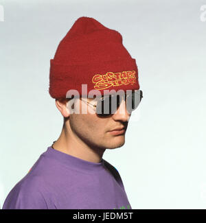 Portrait of a young man in a purple t shirt, wearing a red hat and sunglasses Stock Photo