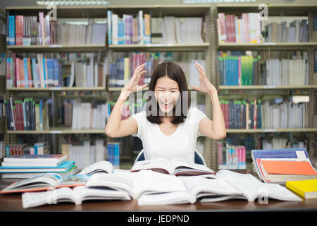 Young Asian student under mental pressure while reading book preparing examination in library at university. Asian student looking stressed. Stock Photo